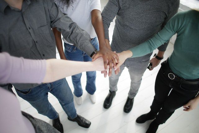 Crop multiracial people joining hands together during break in modern workplace